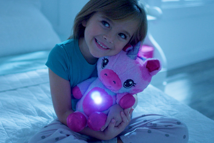 Kind umarmt leuchtendes StarBelly Einhorn Kuscheltier im Bett