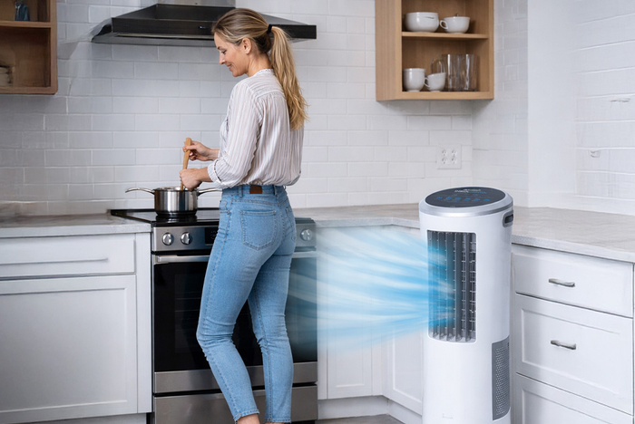 Frau kocht in der Küche während neben ihr das mobile Luftkühlgerät in Funktion ist.