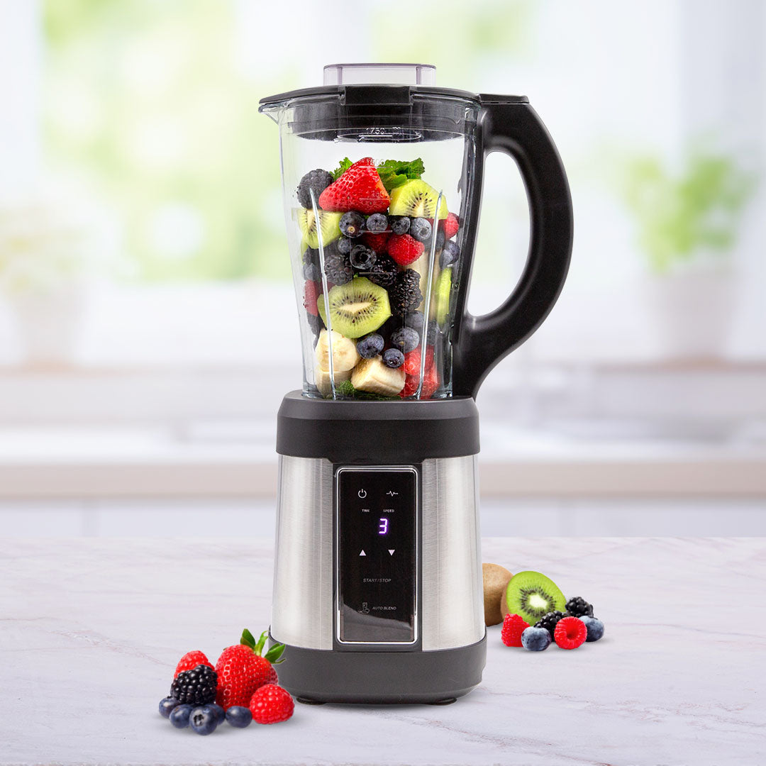 Standmixer mit transparentem Behälter, gefüllt mit frischen Früchten wie Erdbeeren, Kiwi, Beeren und Banane, auf einer Küchenarbeitsplatte.