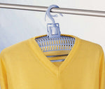 Ein gelbes Shirt hängt auf einem Trockenbügel mit Haken an einer Kleiderstange.