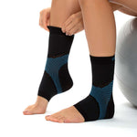 Nahaufnahme von zwei Beinen, auf denen eine Person schwarze, knöchelhohe CopperFit Ice Ankle Sleeve mit blauen Mustern überzieht; sie sitzt dabei neben einem Gymnastikball.