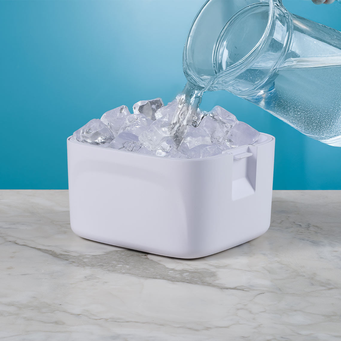 Wasser wird über Eiswürfel in einen weißen Behälter gegossen