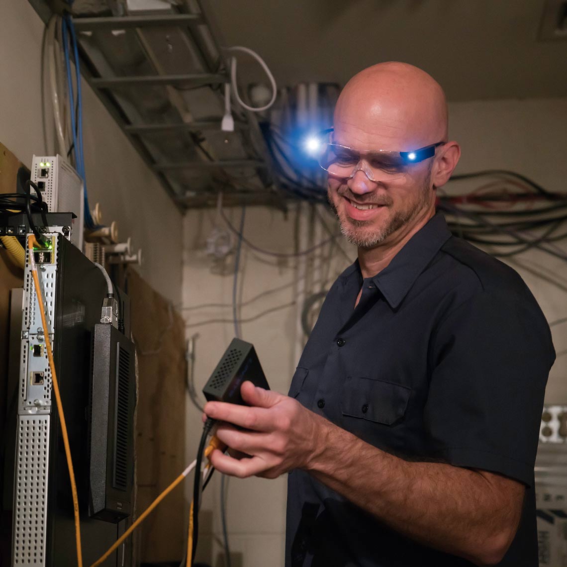 Mann arbeitet mit ZoomMagic LED-Brille und beleuchtet dabei Technikkomponenten im Serverraum.