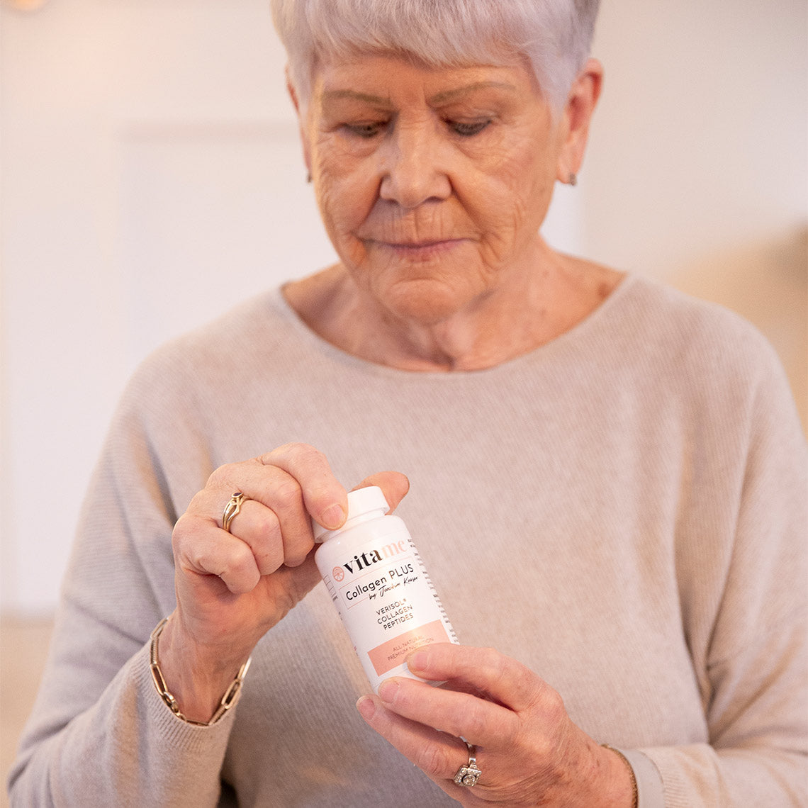 Ältere Frau hält eine Dose Kollagenkapseln in den Händen und betrachtet sie aufmerksam.