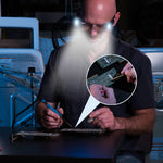 Ein Mann lötet eine Platine mit einer LED-Brille, die den Arbeitsbereich präzise ausleuchtet.