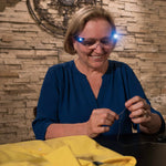Eine Frau fädelt Nadel und Faden ein und trägt dabei eine LED-Brille, die ihr Naharbeitsfeld beleuchtet.