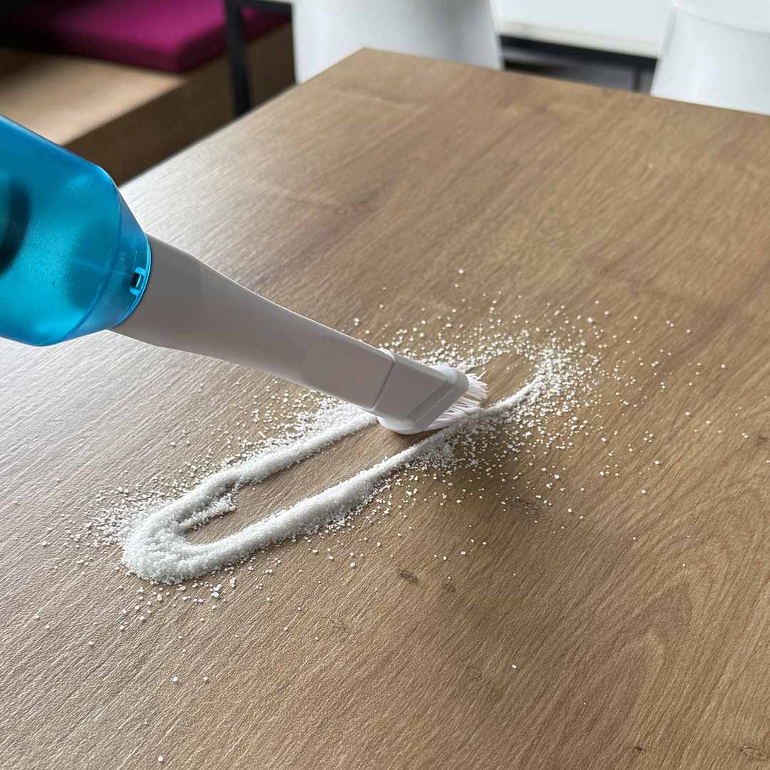 Akku-Staubsauger mit Bürstenaufsatz reinigt Tisch