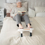 Ältere Frau liegt im Bett, liest ein Buch und nutzt dabei das Fllow Fußmassagegerät zur Entspannung.