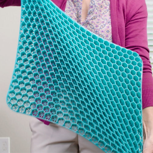 Eine Person hält ein großes, flexibles Gel-Sitzkissen mit elastischer Wabenstruktur – sichtbar biegsam und leicht.