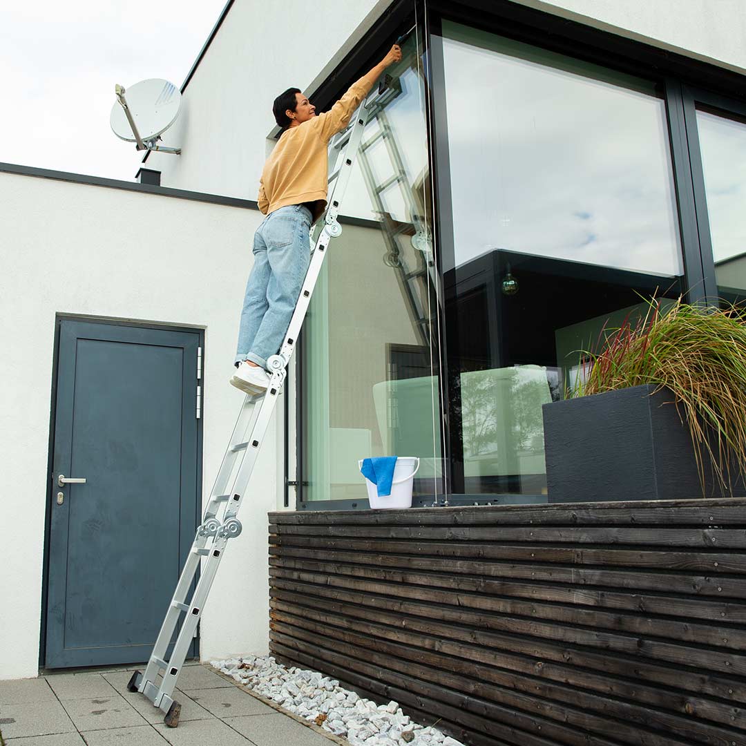 Eine Person nutzt die Hammersmith SuperLadder als Anlegeleiter zum Fensterputzen an der Hausfassade.