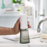 Eine Hand hält den CorpCare MiracleSmile mit gefülltem Wassertank auf einem Waschtisch.