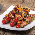 Saftig gegrillte Fleischspieße mit Paprika, Zucchini, Zwiebel und Kirschtomaten auf einem weißen Teller serviert.