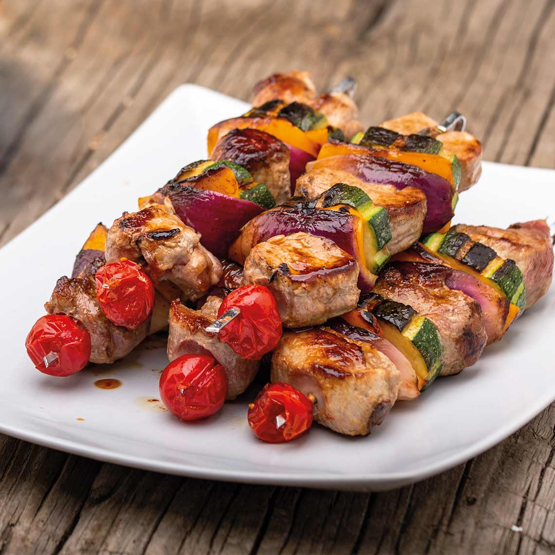 Saftig gegrillte Fleischspieße mit Paprika, Zucchini, Zwiebel und Kirschtomaten auf einem weißen Teller serviert.