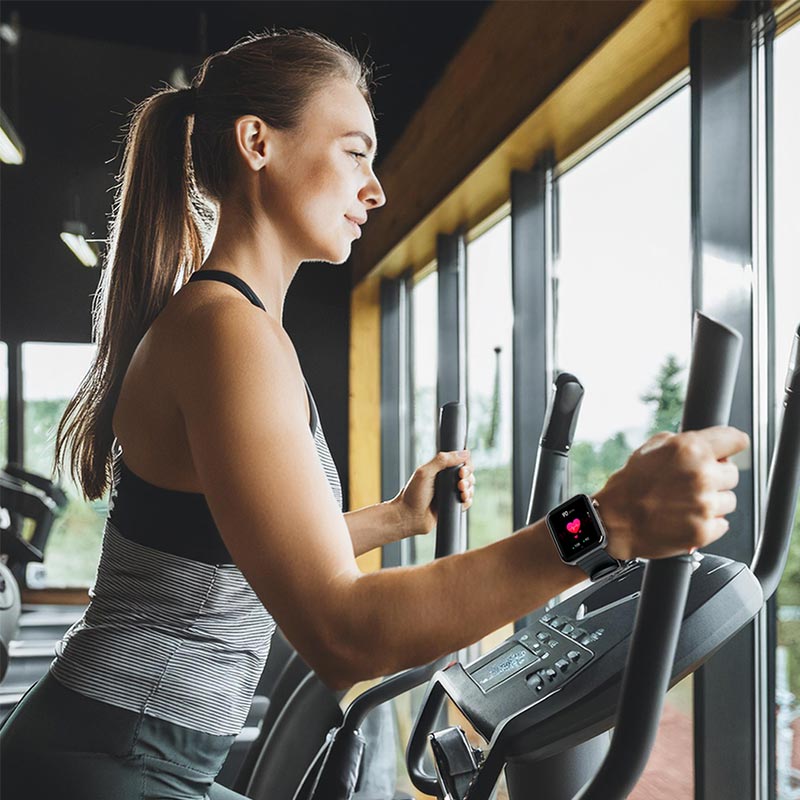 Frau trainiert im Fitnessstudio auf dem Crosstrainer mit dem Kendox LifeTracker zur Pulsmessung am Handgelenk.
