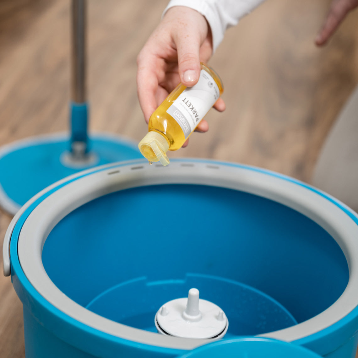 Reinigungsmittel wird in den Eimer des Livington Clean Water Spin Mop auf Holzboden eingefüllt.