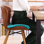 Person sitzt auf flexiblem Gelkissen mit Wabenstruktur auf einem Stuhl am Schreibtisch.
