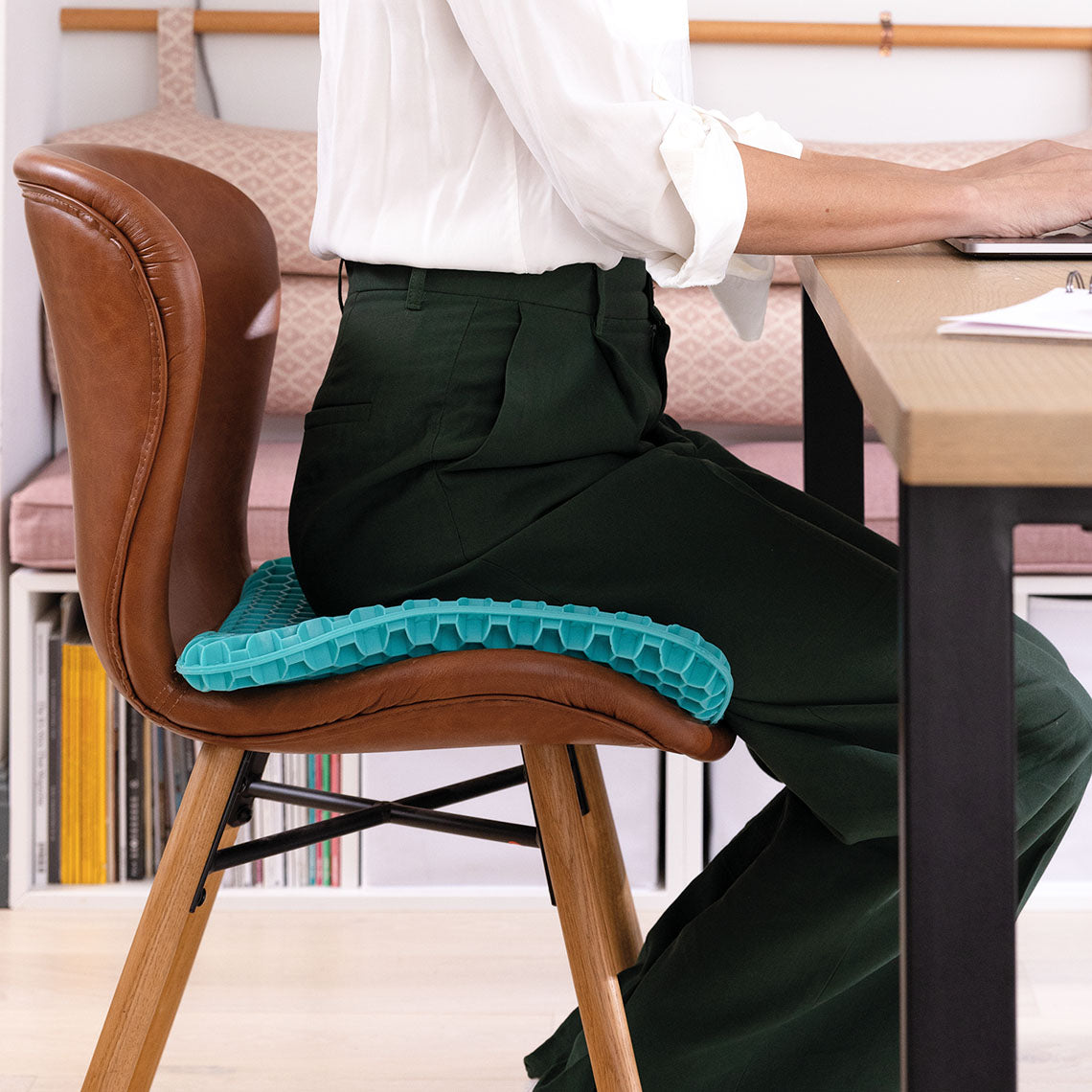 Person sitzt auf flexiblem Gelkissen mit Wabenstruktur auf einem Stuhl am Schreibtisch.