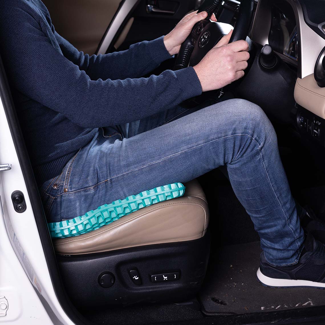 Person sitzt im Auto auf einem Sitzkissen, das den Fahrkomfort verbessert.
