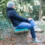 Person sitzt im Park auf einer Bank mit einem Sitzkissen und genießt den Spaziergang.
