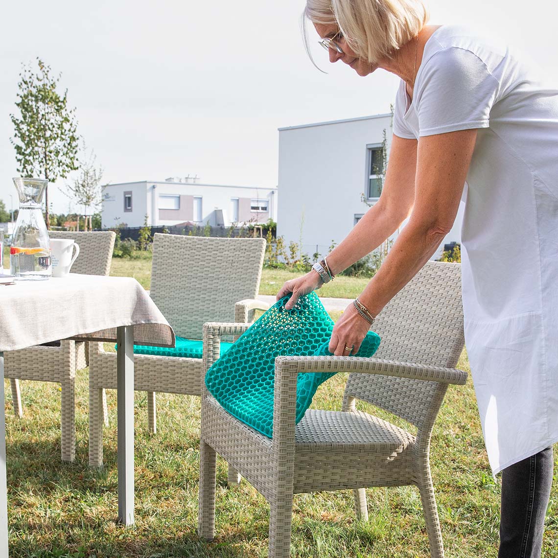 Frau legt ein Sitzkissen auf einen Gartenstuhl im Außenbereich.