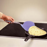 Ein Pfannenwender hebt einen Crêpe aus einer Pfanne auf einem Kochfeld.