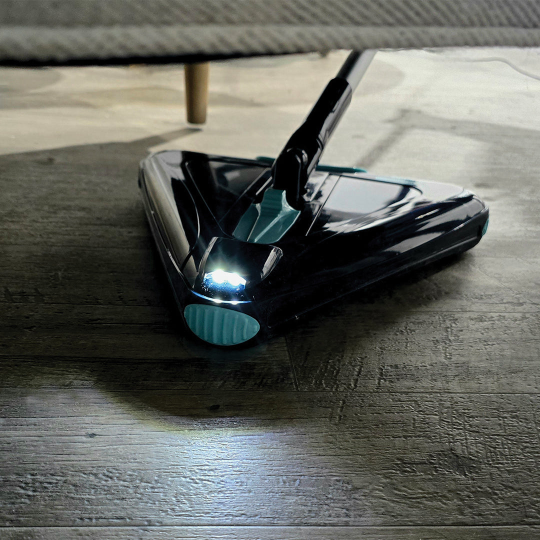 Ein dreieckiger Bodenreiniger fährt unter ein Möbelstück und beleuchtet den Boden dank integriertem LED-Licht, um Staub und Schmutz in dunklen, schwer erreichbaren Bereichen sichtbar zu machen.