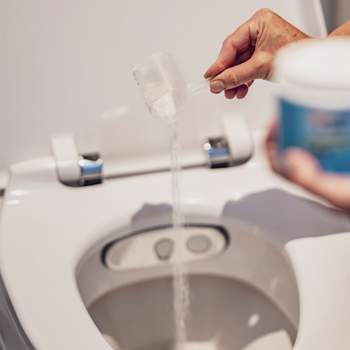 Eine Hand schüttet  FoamFlush Aktivreinigungsschaum-Pulver mit einem Messlöffel in eine Toilette.