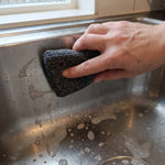 Eine Hand reinigt mit dem Livington ForeverSponge Spülschwamm eine Edelstahl-Spüle mit Seifenschaum.