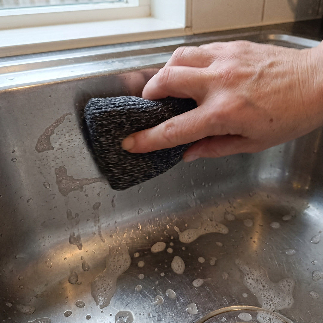 Eine Hand reinigt mit dem Livington ForeverSponge Spülschwamm eine Edelstahl-Spüle mit Seifenschaum.