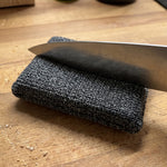 Livington ForeverSponge Schwamm auf einer Holzoberfläche, auf den eine scharfe Messerklinge drückt, um das robuste  Material zu demonstrieren.