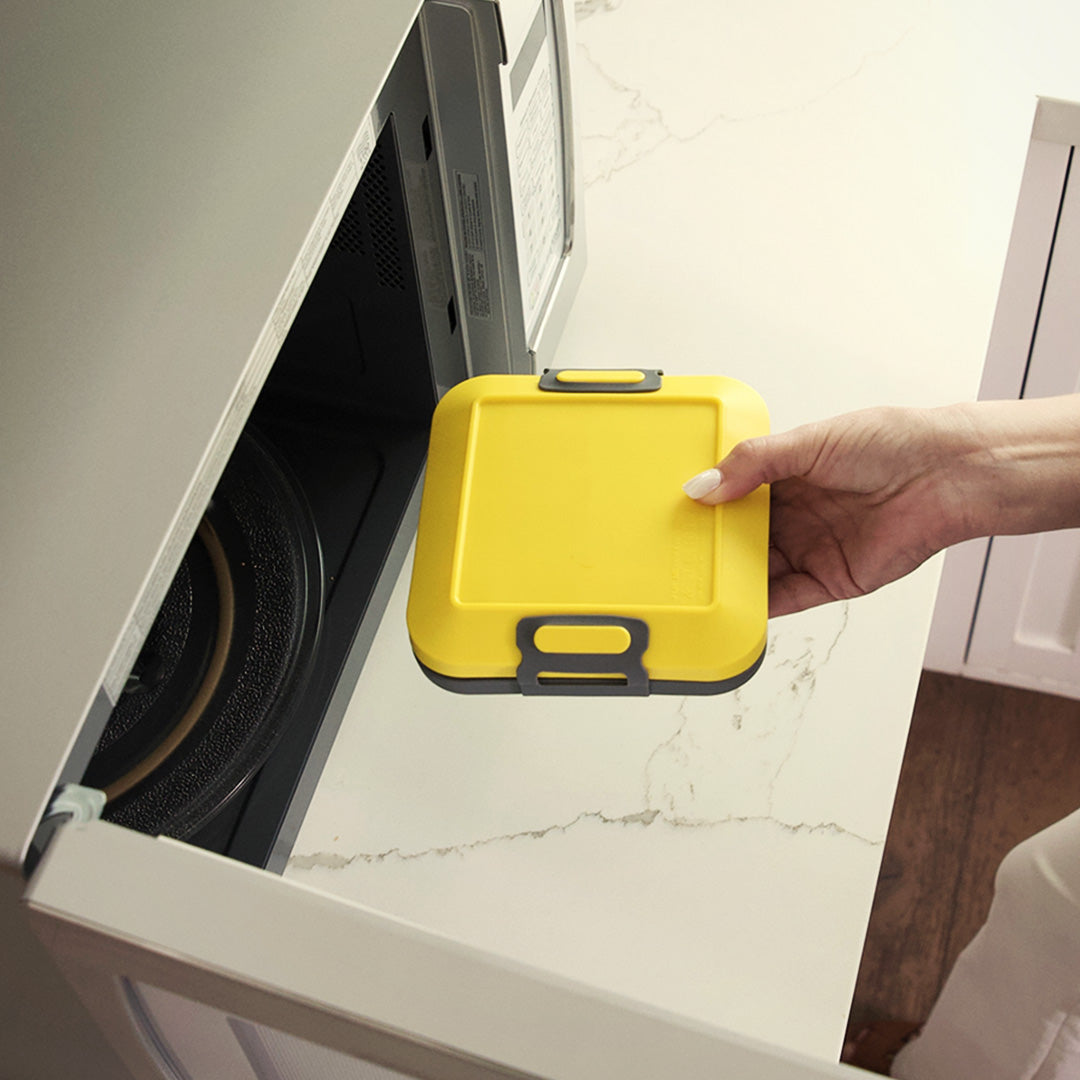 Eine Hand platziert den Toastie Mikrowellen-Toaster in einer geöffneten Mikrowelle.