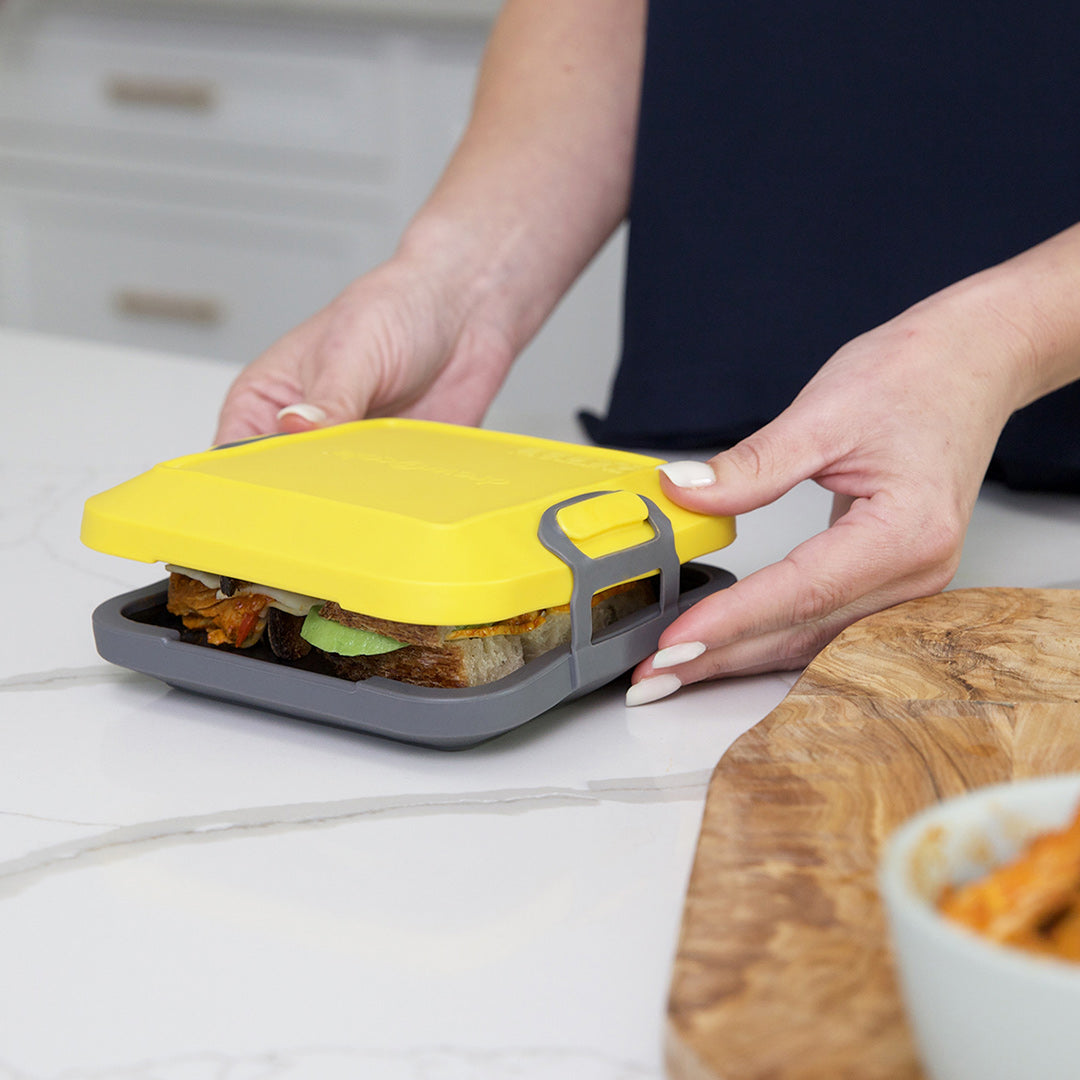 Eine Person hält den Livington Toastie Mikrowellen-Toaster, in dem ein belegtes Sandwich für die Zubereitung in der Mikrowelle liegt.