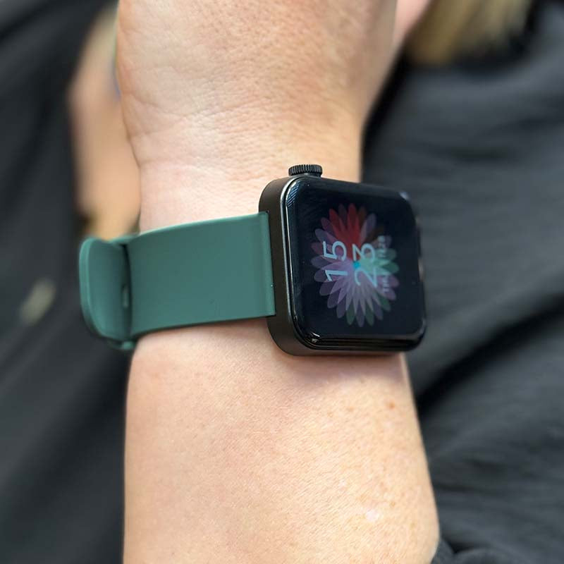 Eine Smartwatch mit dunkelgrünem Armband ist am Handgelenk einer Person zu sehen. Auf dem Display wird eine farbige Blume angezeigt.