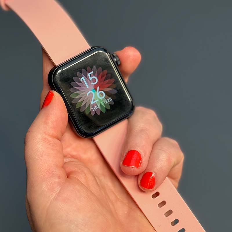 Smartwatch mit rosafarbenem Armband wird in der Hand gehalten, Display zeigt Uhrzeit an.