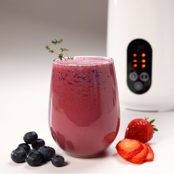 Glas mit frischem Beeren‑Smoothie, daneben Erdbeeren und Heidelbeeren, im Hintergrund ein Pflanzendrink‑Maker.