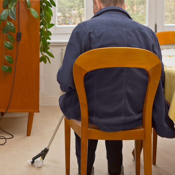 Mit der Greifhilfe wird sitzend ein Gegenstand vom Boden aufgehoben, ohne sich bücken zu müssen