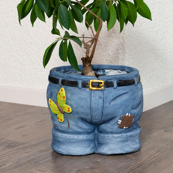 Pflanzentopf in Form einer Hose mit Schmetterling und Gürtel, bepflanzt mit einer grünen Zimmerpflanze.