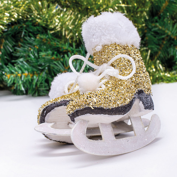 Ein gold-glitzernder Schlittschuh mit Fellbesatz als festlicher Dekoanhänger vor grünem Tannenschmuck.