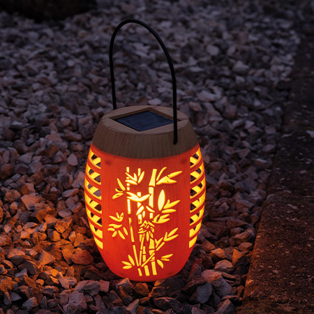 Solarbetriebene Laterne in Bambusoptik mit filigranem Bambus-Motiv und warmweißem Licht, leuchtend im Dunkeln auf Kieshintergrund