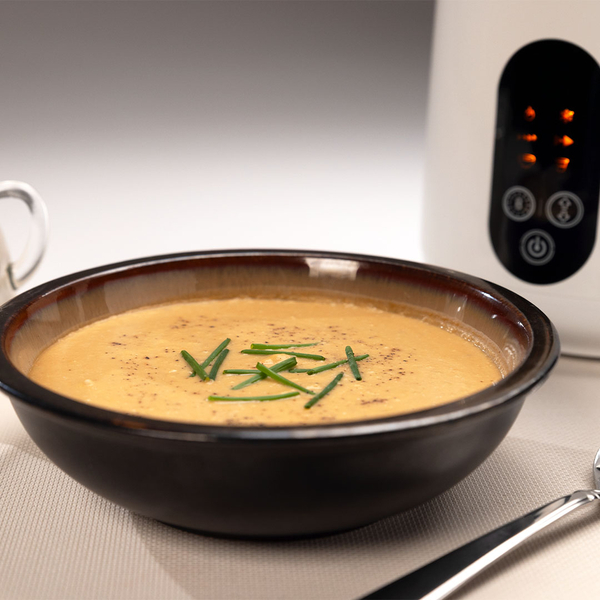 Suppenteller mit Suppe garniert mit Schnittlauch, dahinter der Pflanzendrinkmaker.